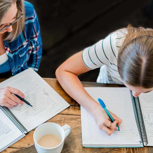 Parent instructing child writing in a notepad